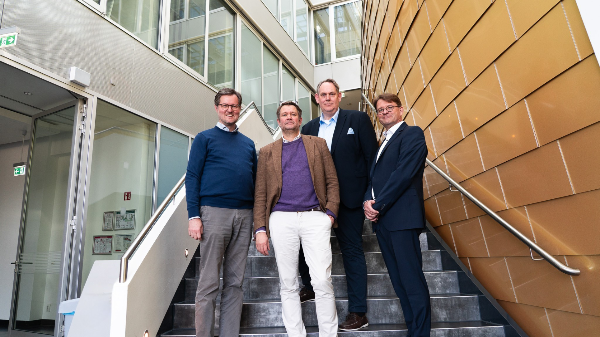 Three people stand oindoors on a staircase.